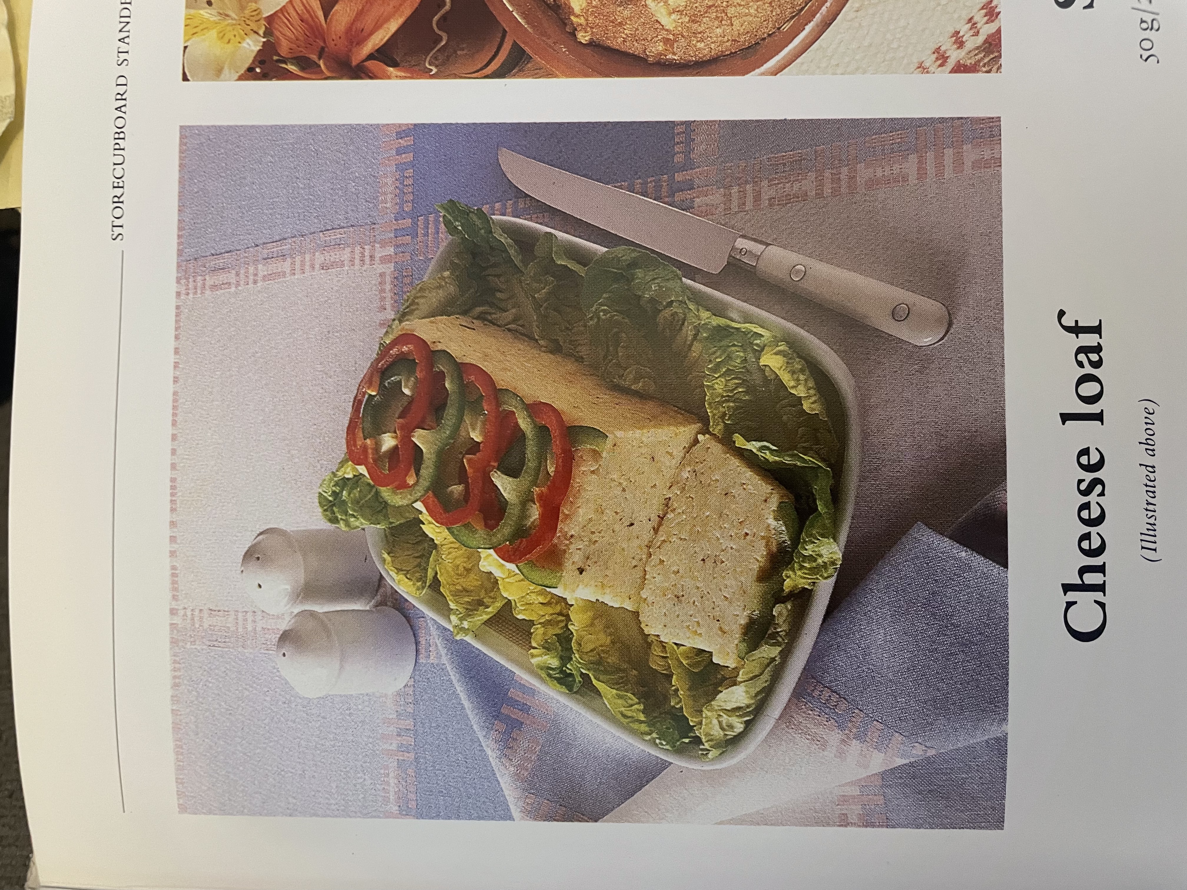 A cookbook photo of a Cheese Loaf, which is a loaf-shaped white mush on a bed of lettuce leaves, topped with bell pepper slices.