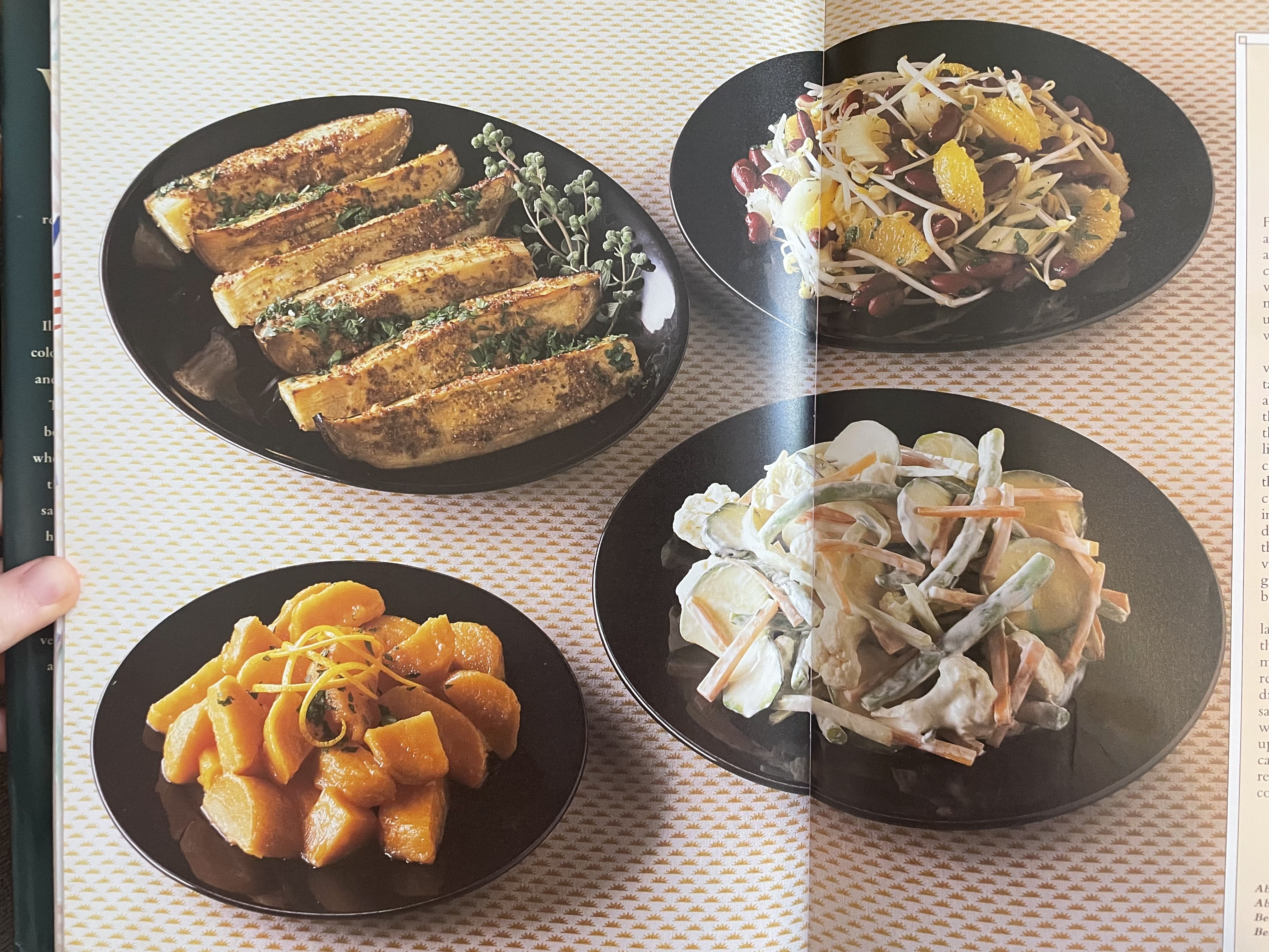 Four plates of food (two salads, two vegetable sides) in round black dishes sitting on a tablecloth decorated with small orange sunrises in a regular pattern.