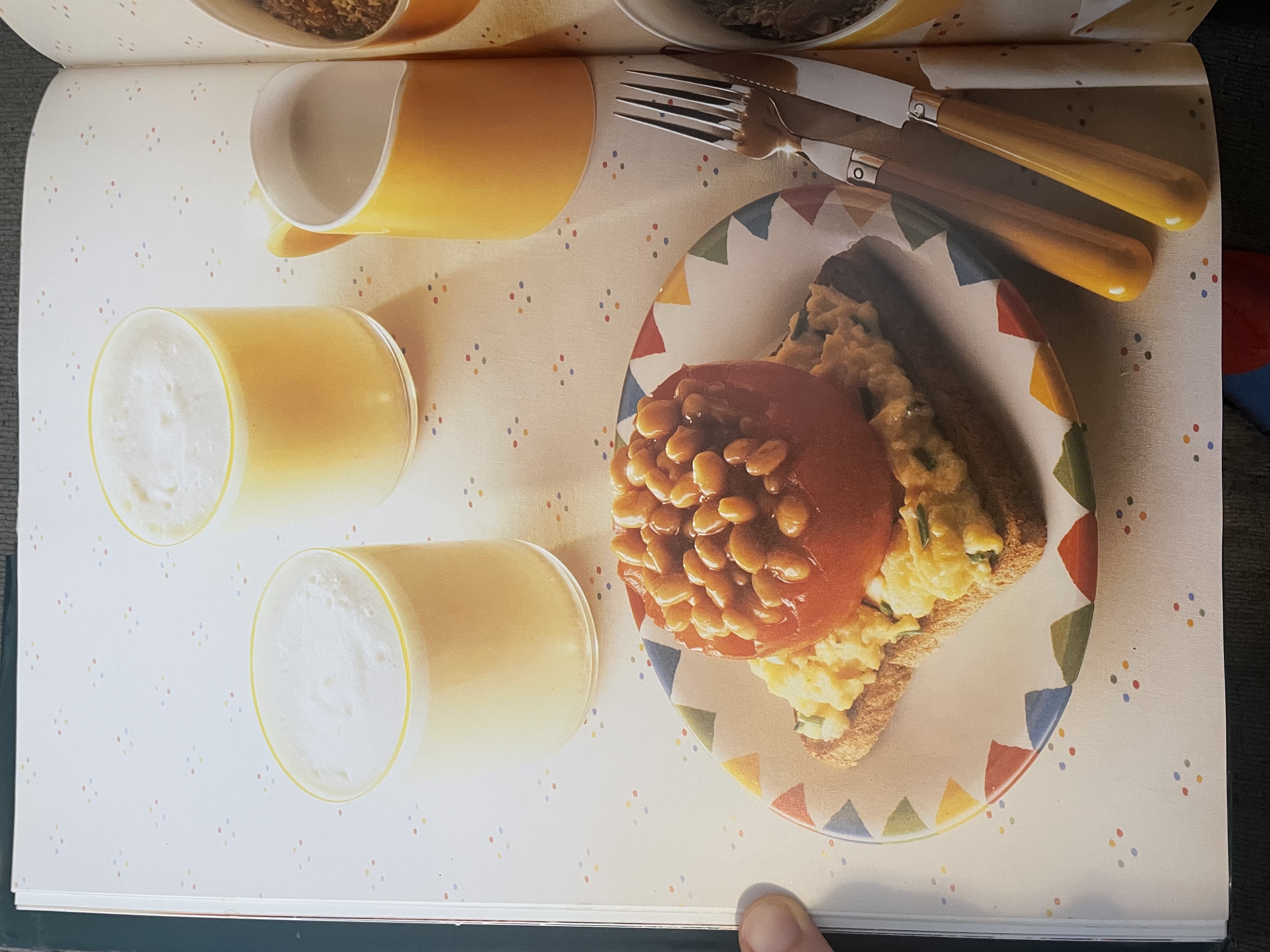 A cookbook photo of a slice of toast with scrambled eggs on top, and on top of the scrambled eggs is half of a hollowed-out tomato filled to the brim with baked beans